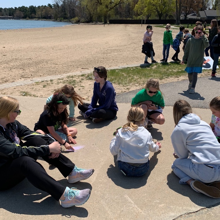high school students help elementary students with chalk drawings by the pier